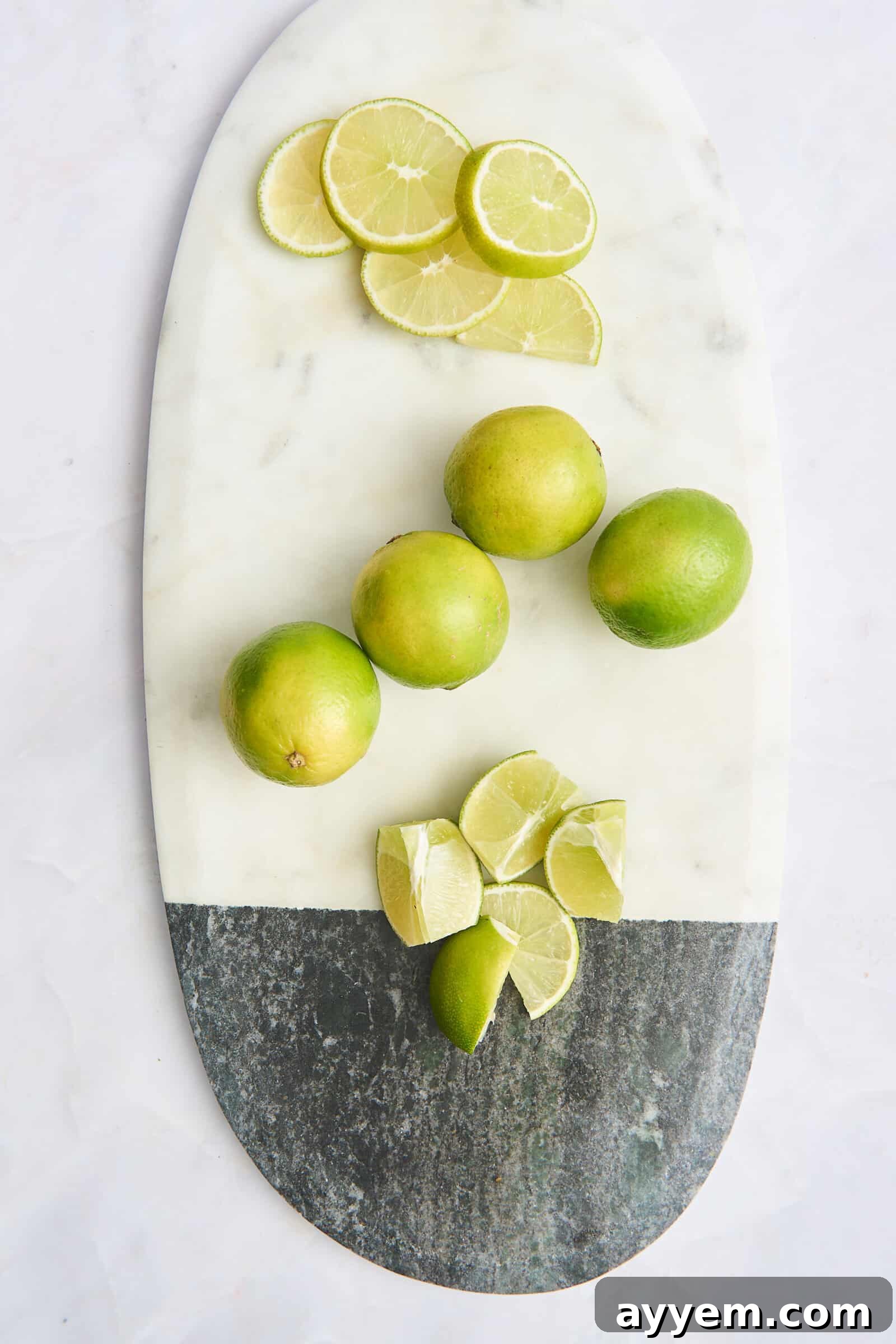 Lime rounds, whole limes, and lime wedges on a cutting board, prepared for use.