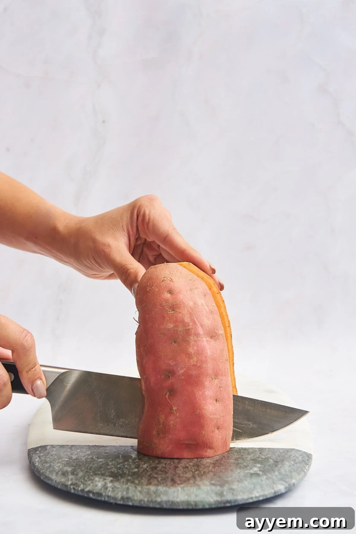A sweet potato being sliced in half lengthwise on a wooden cutting board.
