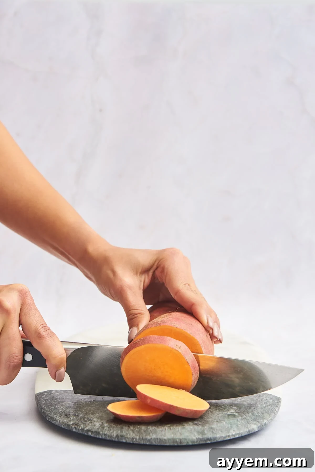 A sweet potato being sliced into perfect rounds on a cutting board.