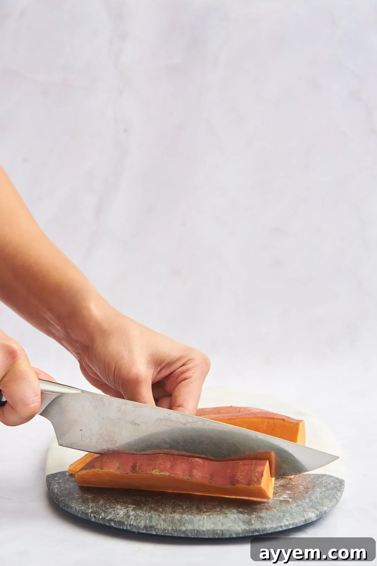 A sweet potato being sliced into uniform sticks for fries.