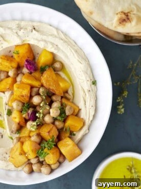 A bowl of roasted maple butternut squash hummus dip, elegantly presented with olive oil and warm pita bread on the side.