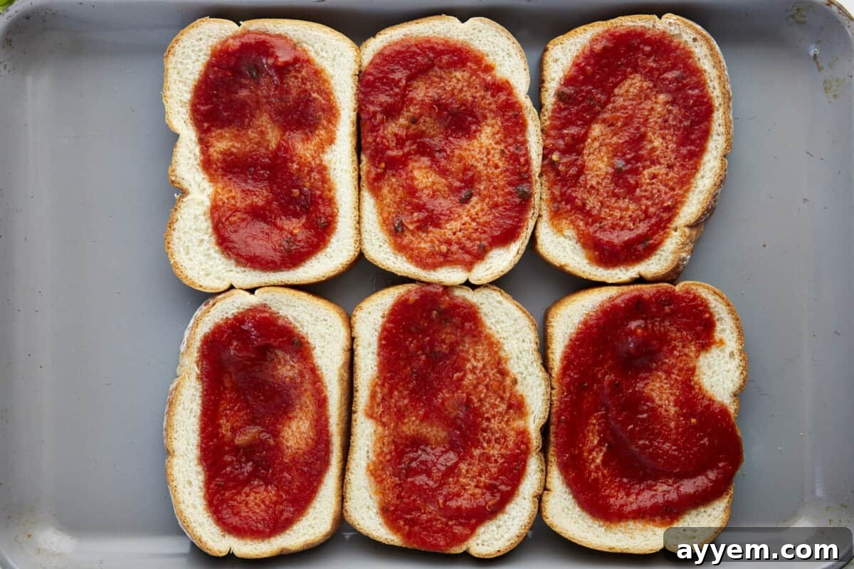 Marinara spread over six pieces of bread on a sheet pan.