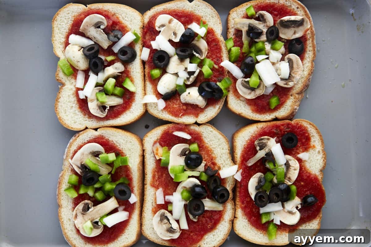 Marinara spread over pieces of bread topped with mushrooms, onions, and peppers on a sheet pan.