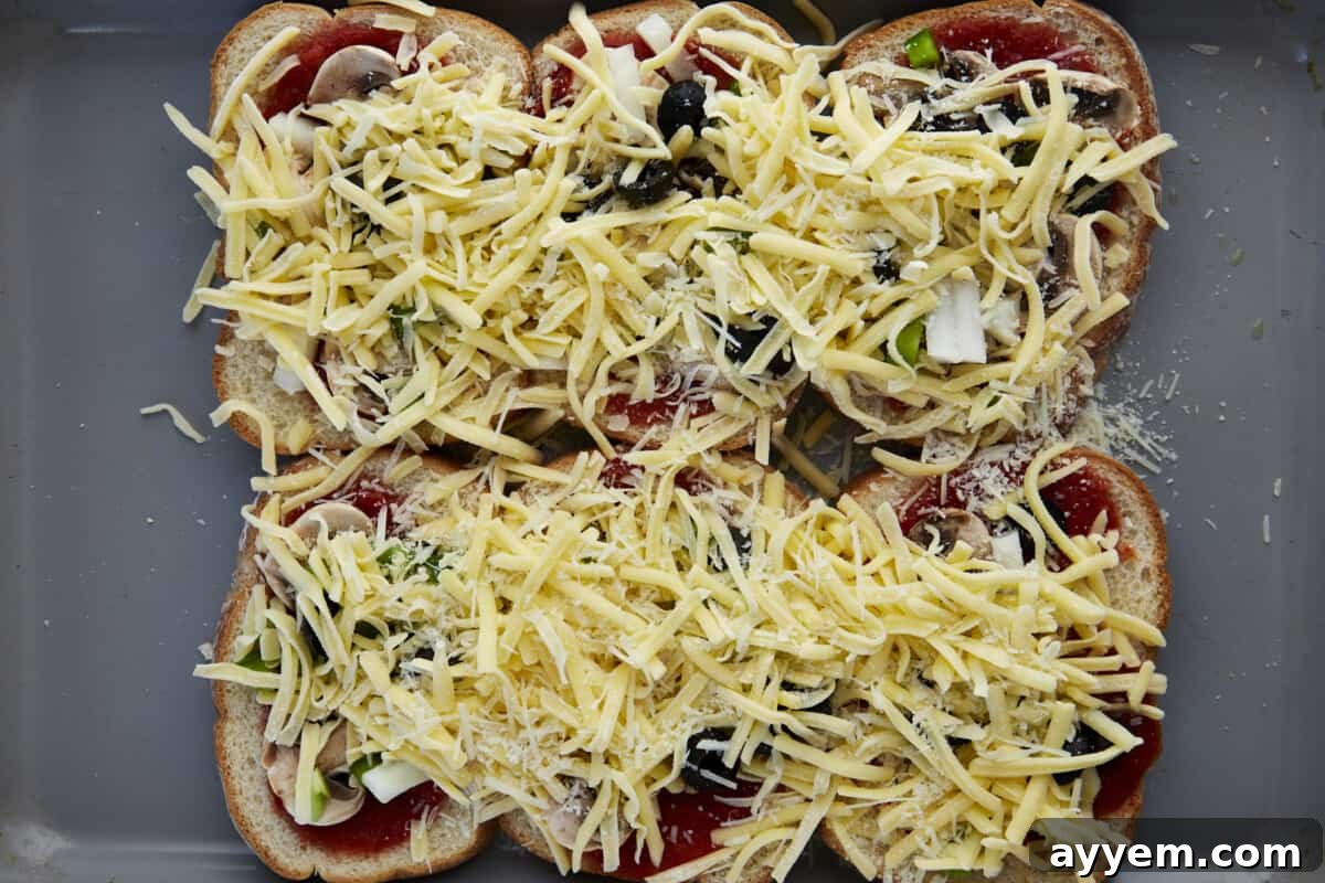 Shredded cheese sprinkled over slices of bread topped with marinara, peppers, onions, and mushrooms on a baking sheet, ready for the oven.