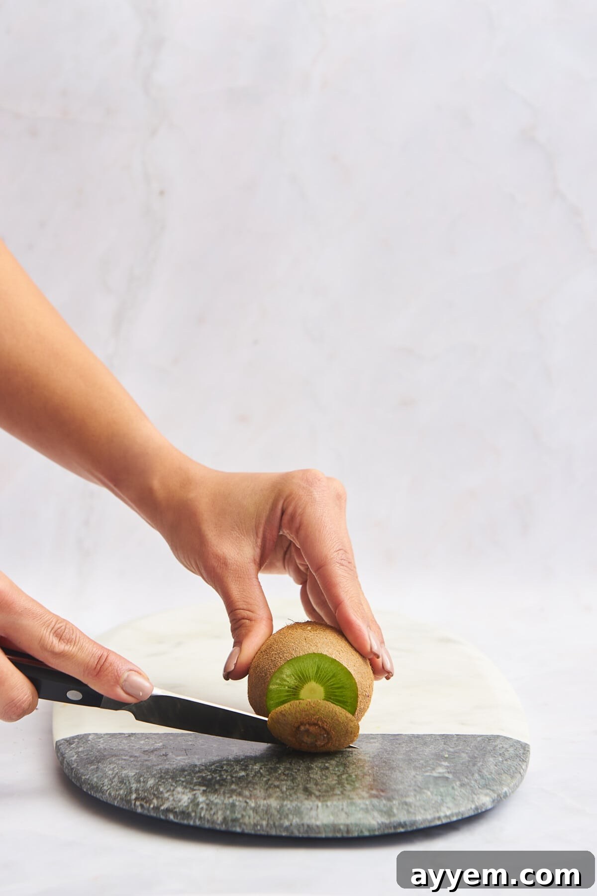 Slice Your Kiwi Like a Pro 3 The end of a kiwi being trimmed with a knife, demonstrating the first step in preparing the fruit for various cuts.