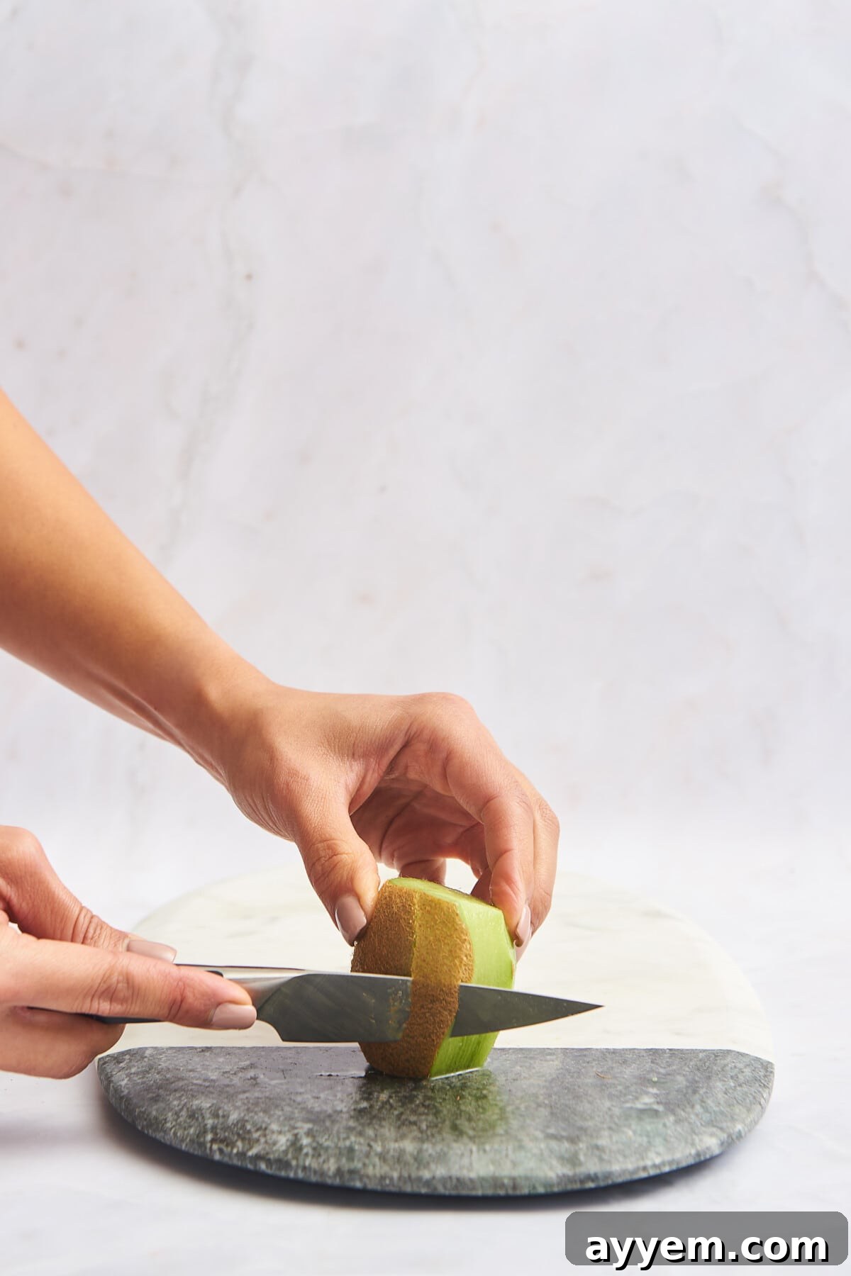 Slice Your Kiwi Like a Pro 4 A sharp knife carefully removing the fuzzy skin from a kiwi, illustrating a common peeling method.