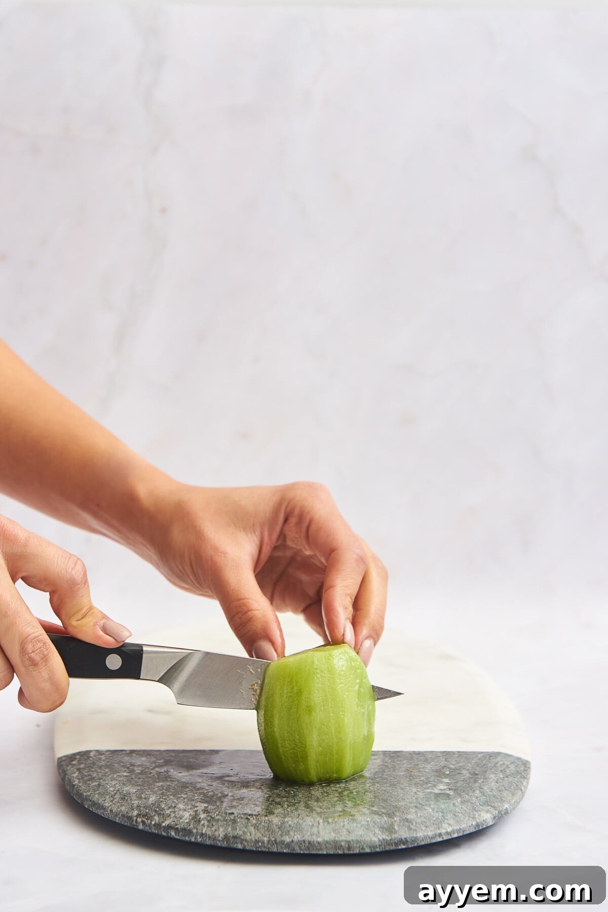 Slice Your Kiwi Like a Pro 7 A hand using a knife to slice a skinless kiwi in half, demonstrating preparation for quarters or cubes.