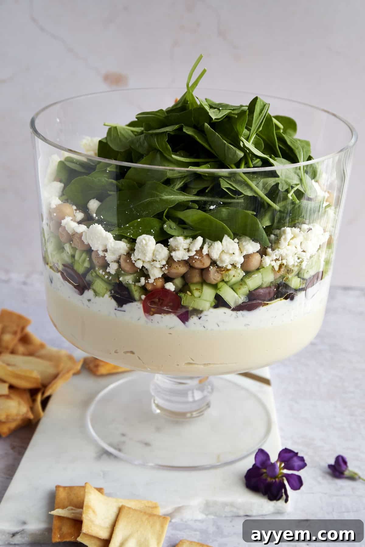 A close-up shot of the finished 7 Layer Greek Dip in a trifle bowl, highlighting the colorful and distinct layers.
