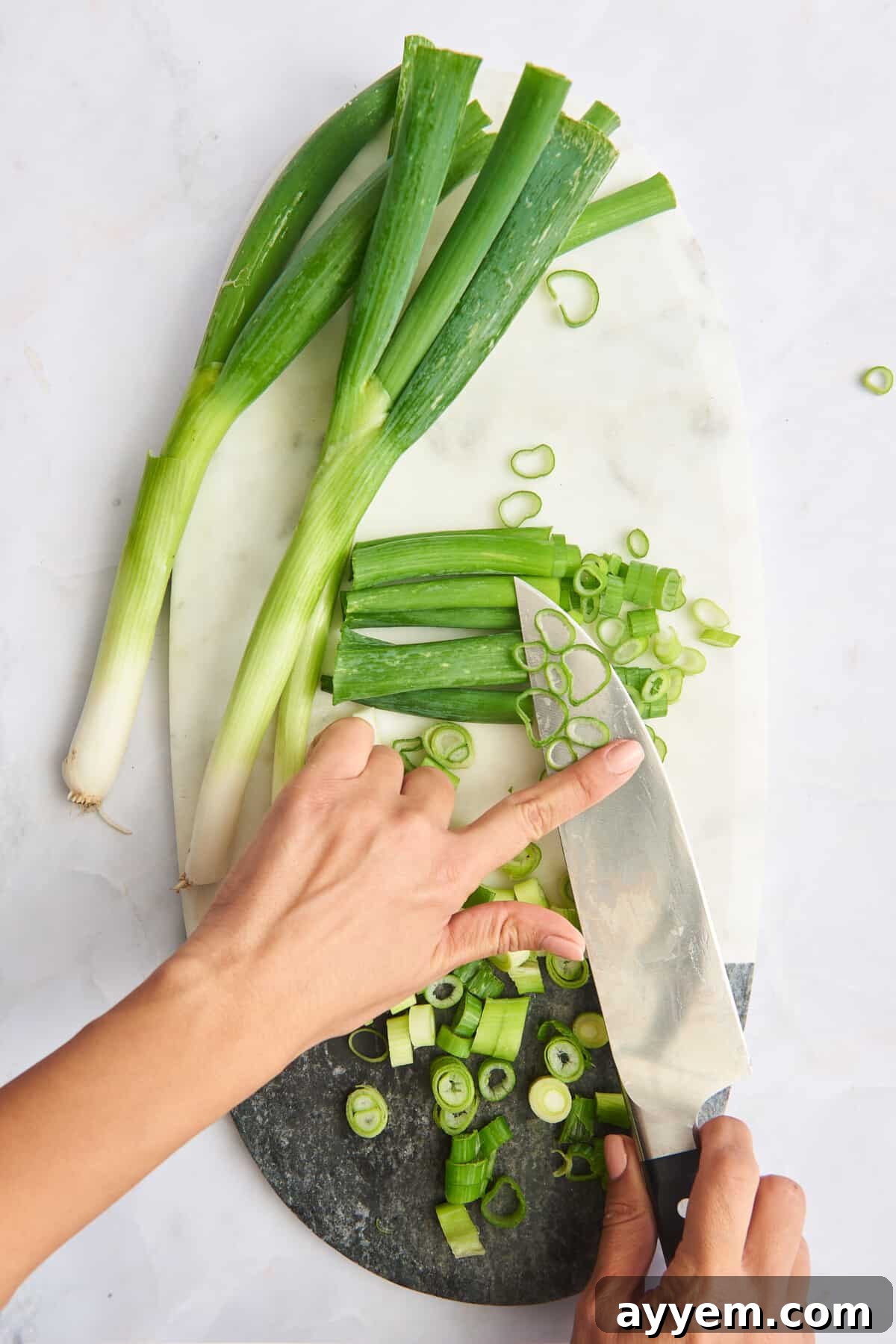 A sharp knife and freshly chopped scallions on a wooden cutting board, alongside whole green onions, ready for culinary use.