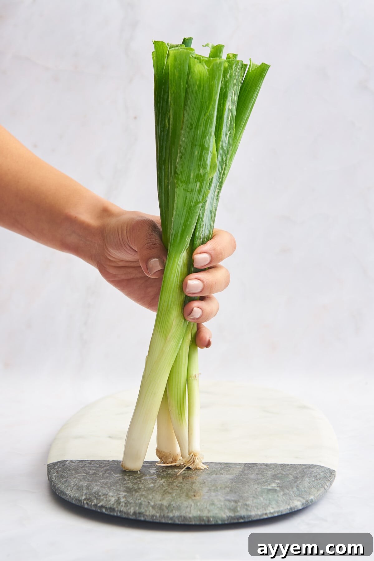 A hand holding a vibrant bunch of fresh green onions over a wooden cutting board, ready for preparation.