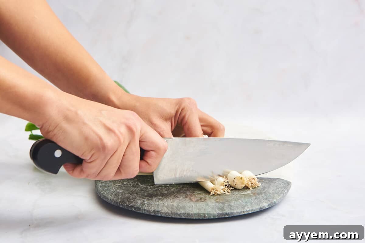 Two hands slicing the white ends off a bunch of scallions.