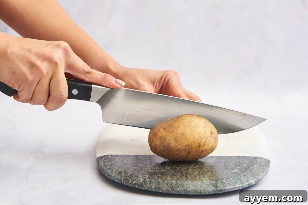 A skilled hand precisely slicing a potato in half on a wooden cutting board, demonstrating the initial step for various potato cuts.