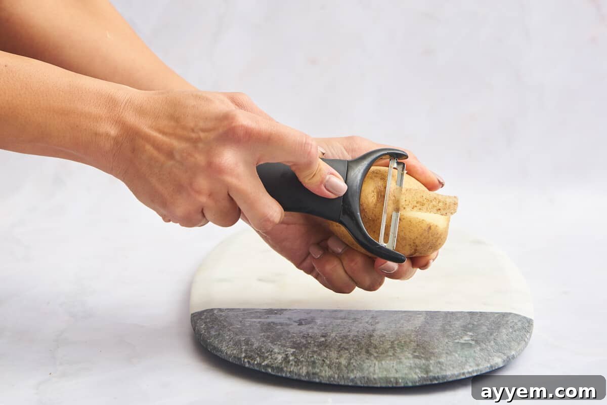 A potato being peeled expertly with a vegetable peeler, showcasing the removal of its outer skin.
