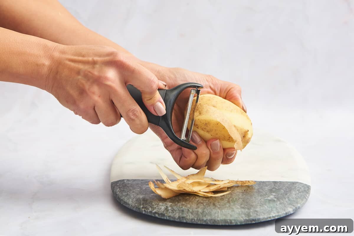Close-up of a potato being peeled with a vegetable peeler, emphasizing the smooth technique and preparation.