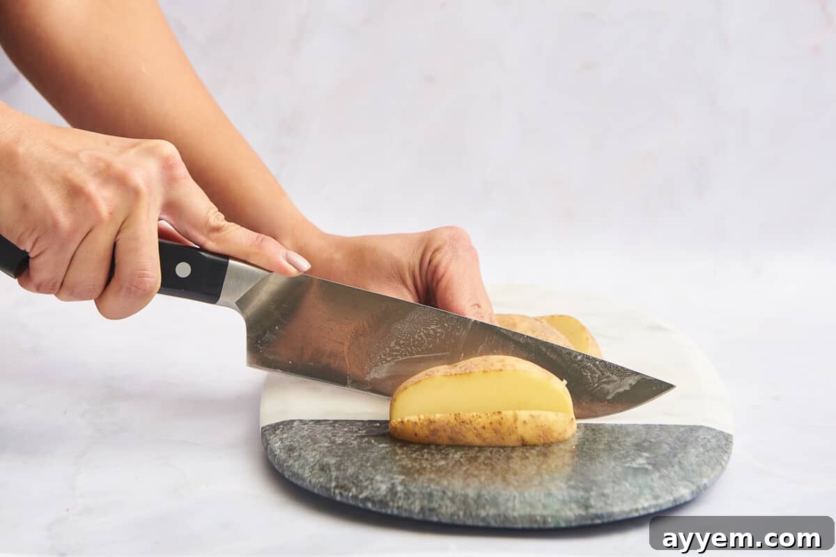 A potato being cut into uniform slices on a cutting board, a precursor to making fries or cubes.