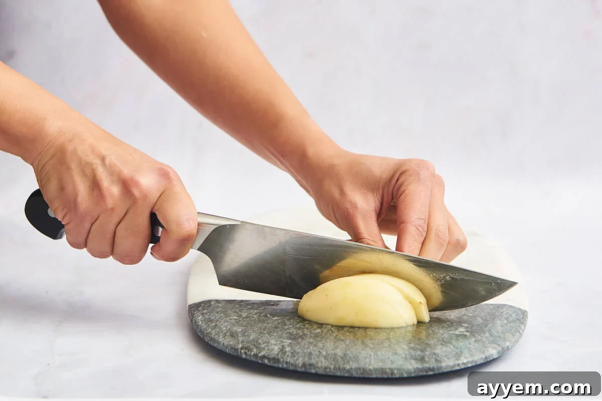 A peeled potato being sliced into long, even strips suitable for making fries, demonstrating precision.
