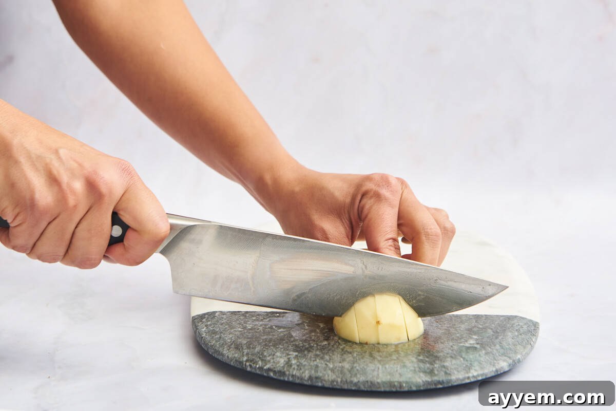 A peeled potato being meticulously cut into uniform cubes on a cutting board, ready for cooking.