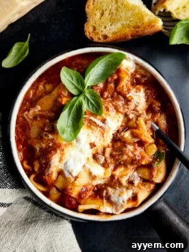 A spoon sticking out of a bowl of rich lasagna soup topped with fresh basil, ready to be enjoyed.