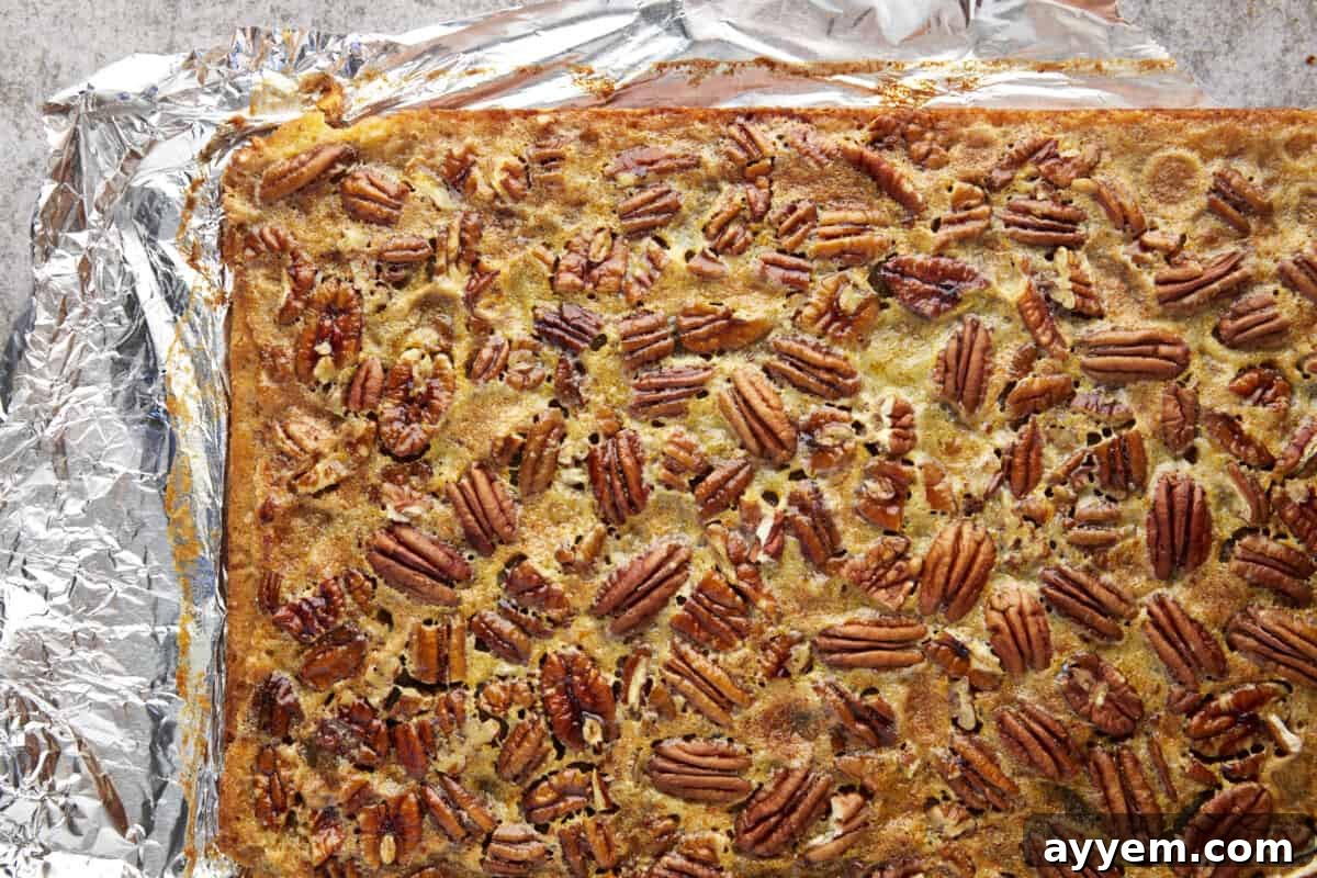 A slab of easy pecan pie bars on top of aluminum foil, ready for cutting into perfect squares.