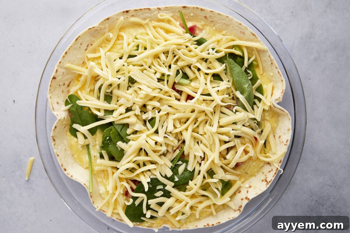 Cheese and veggies over an unbaked egg and cottage cheese mixture over a tortilla in a round dish. 