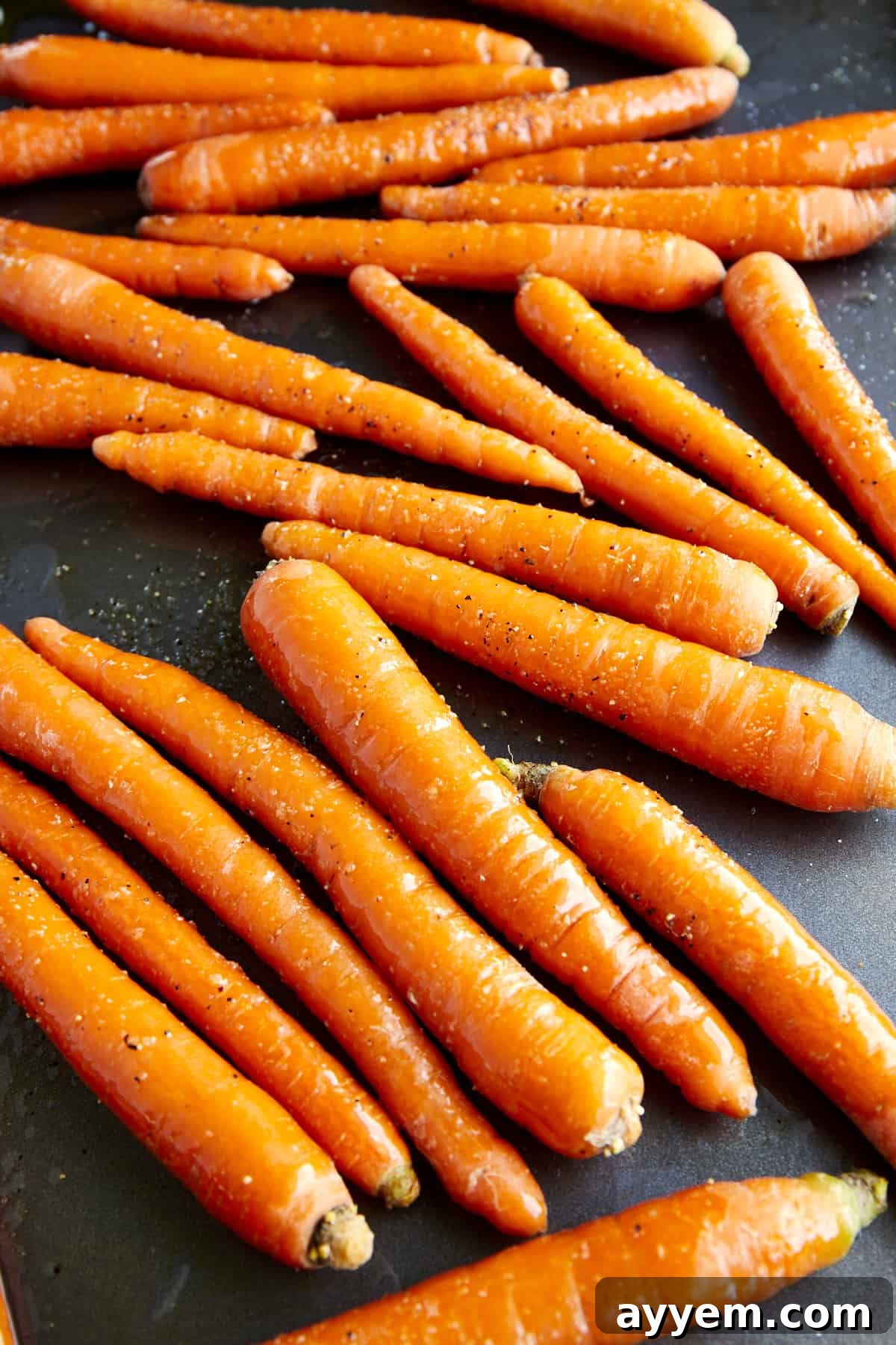 Unbaked carrots, evenly spaced on a baking sheet, ready for roasting.