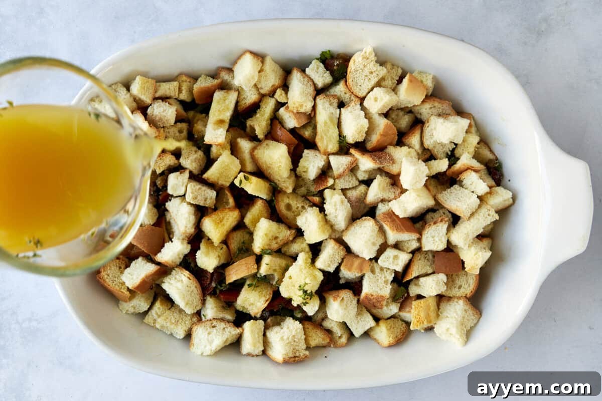 Chicken broth being poured over bread stuffing in a baking dish.