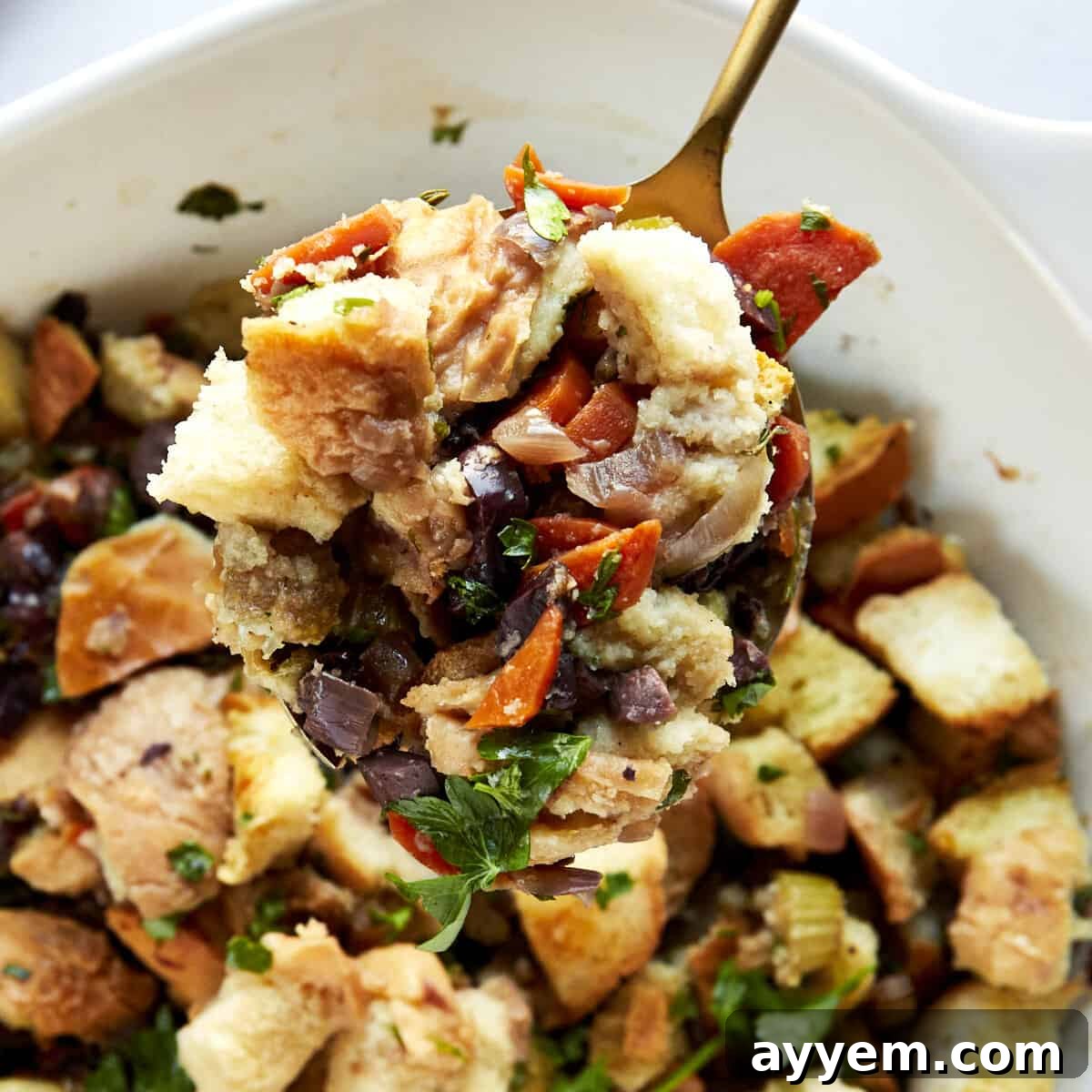 A spoon lifting a scoop of Mediterranean style stuffing from a baking dish.
