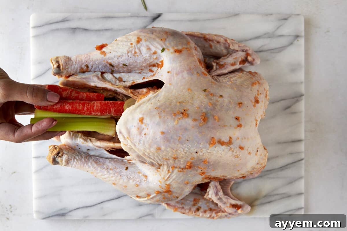 Celery and carrot sticks being placed inside the turkey for steaming and flavoring.