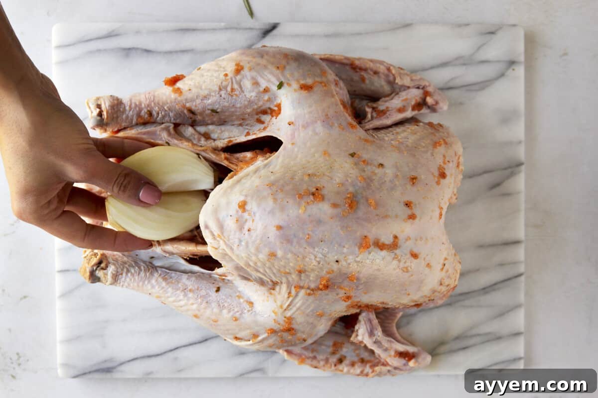 Placing an onion half into the turkey cavity for aromatic infusion.