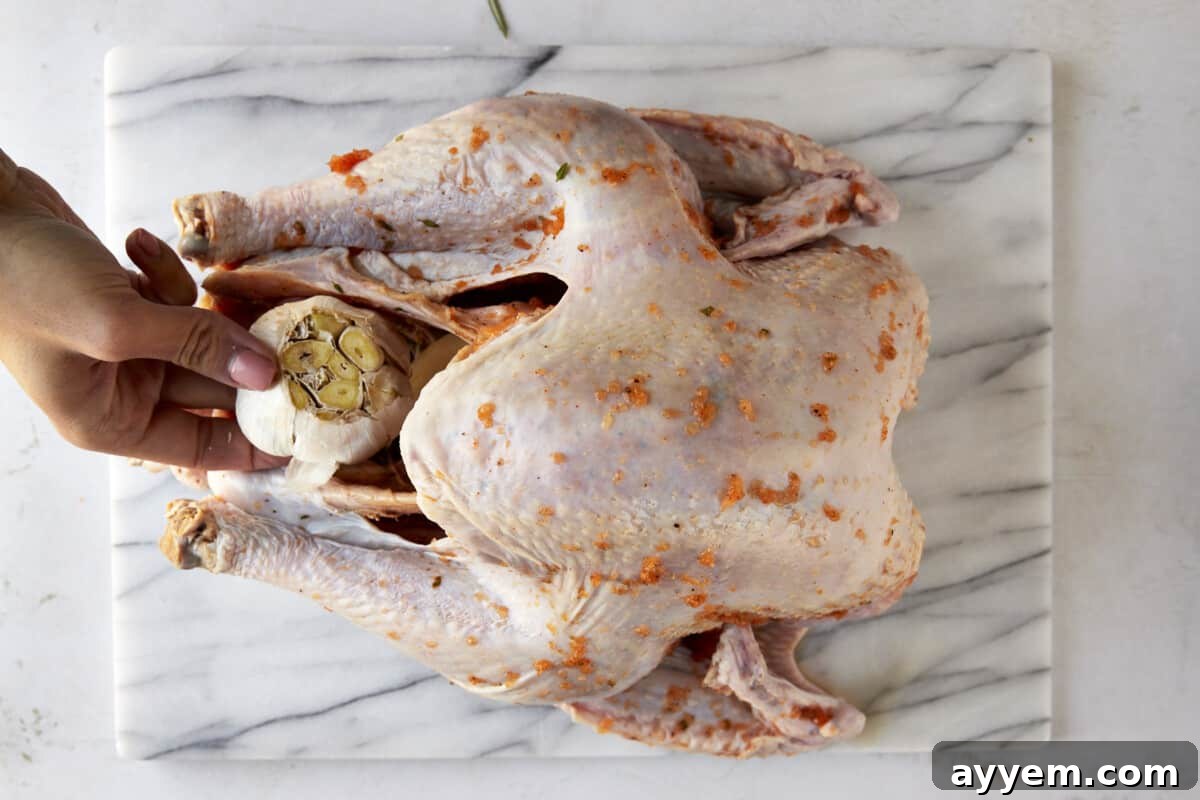 A head of garlic being added to the turkey cavity to enhance flavor.