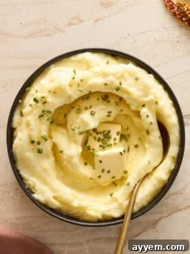 A bowl of creamy mashed potatoes, adorned with melting butter and fresh chives, ready to be served.