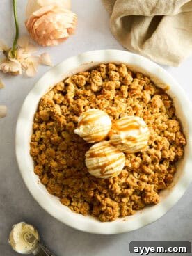 A warm apple crisp topped with a generous scoop of vanilla ice cream and a drizzle of caramel sauce.