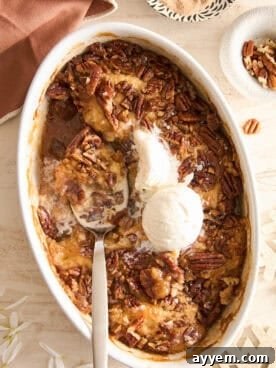 An oval baking dish filled with warm, bubbling pecan cobbler, topped with two scoops of vanilla ice cream.