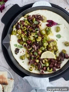 A warm feta dip, glistening with savory olive oil and topped with marinated olives, ready to be served.