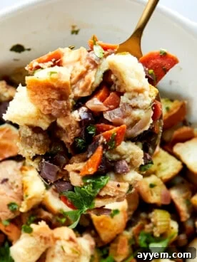 A serving spoon lifting a scoop of savory Mediterranean-style bread stuffing from a baking dish.