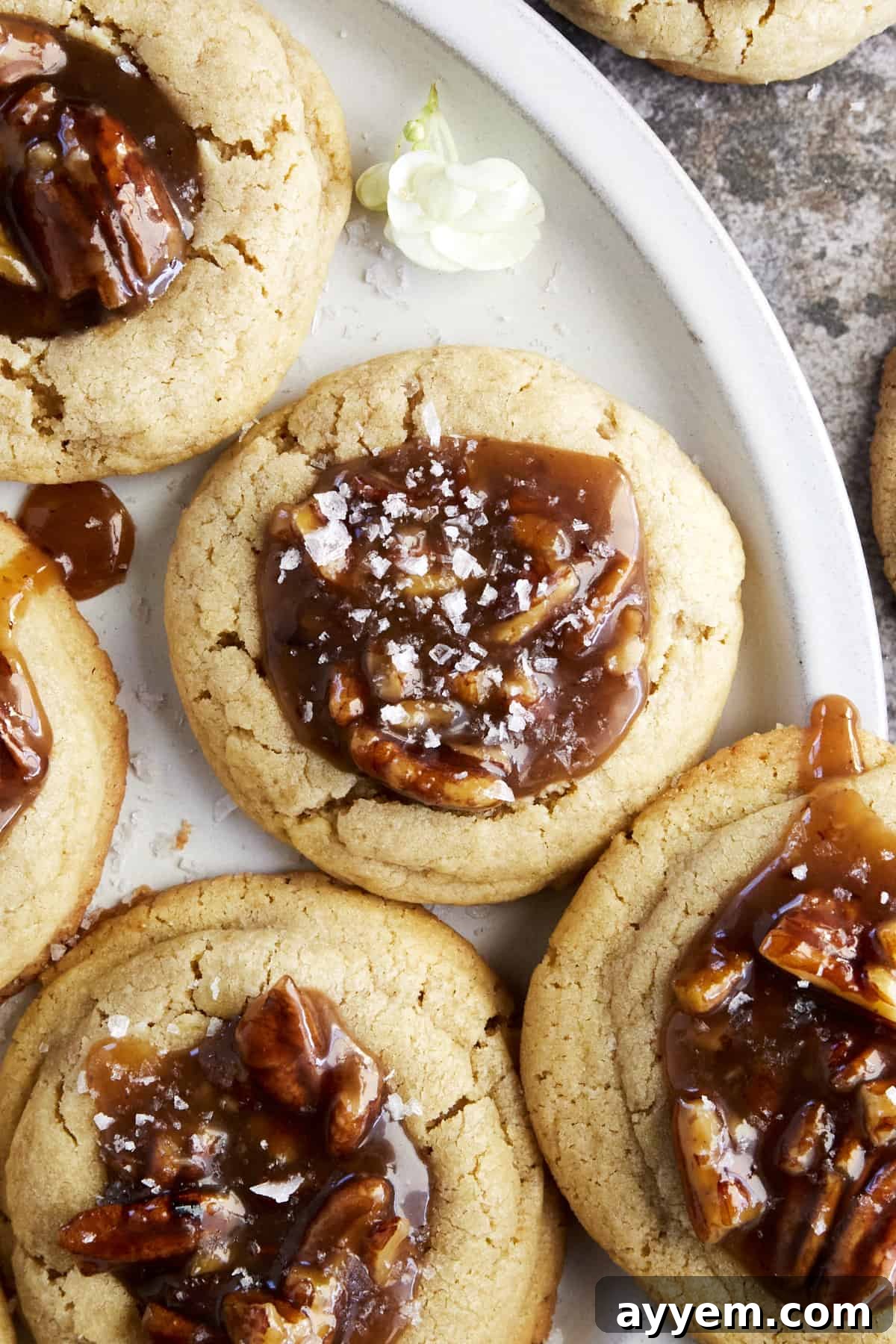 A plate of freshly baked Pecan Pie Cookies, each perfectly formed with a generous dollop of pecan topping and a sprinkle of flaky sea salt.
