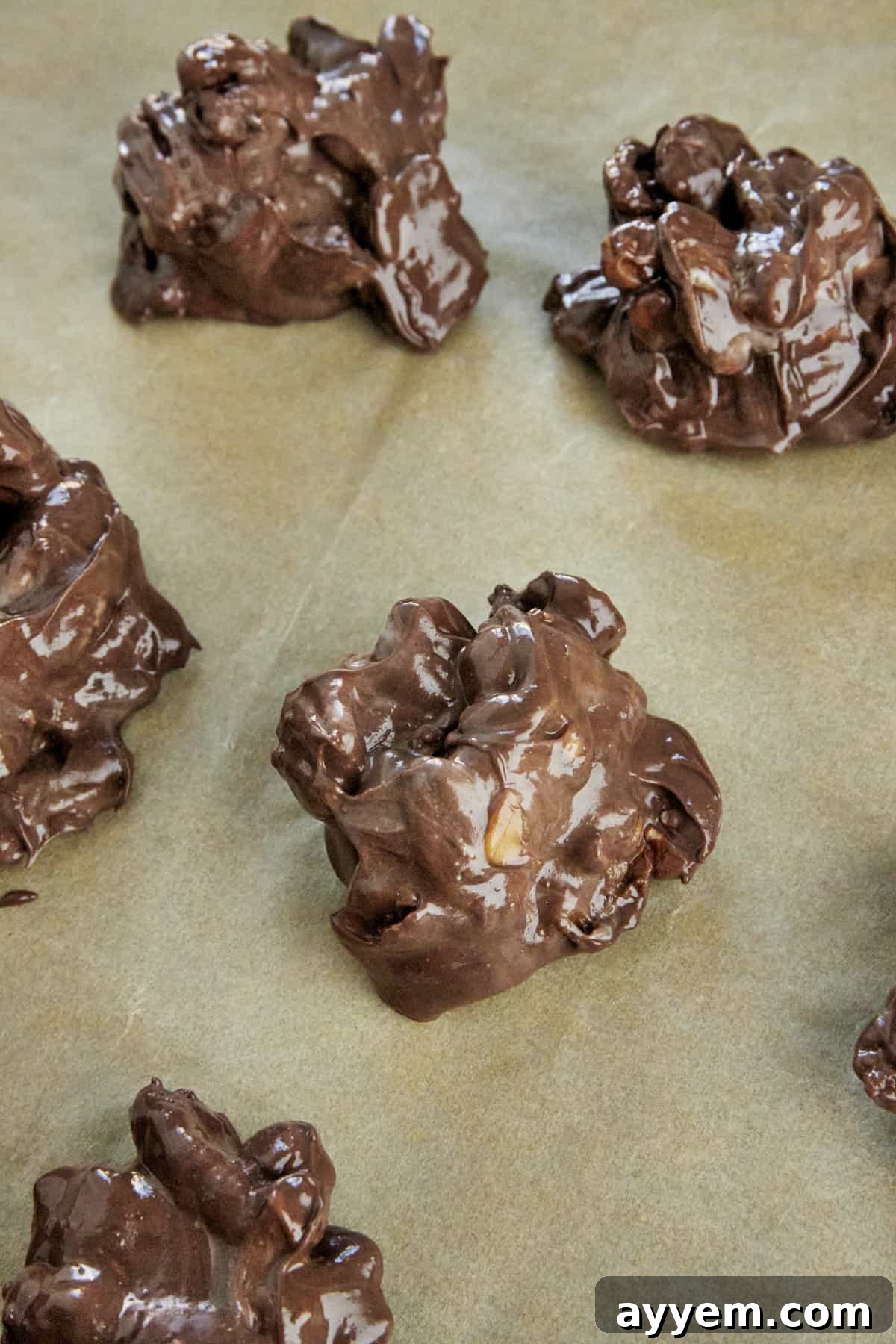 Freshly portioned hot caramel pecan clusters shimmering on a parchment-lined baking sheet, awaiting cooling.