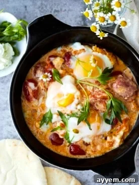 An overhead shot of a skillet filled with golden oven-baked eggs, crumbled feta cheese, and colorful vegetables.