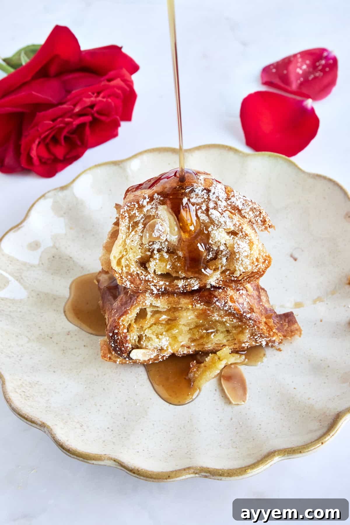 Maple syrup being drizzled generously over a piece of almond croissant French toast on a plate.
