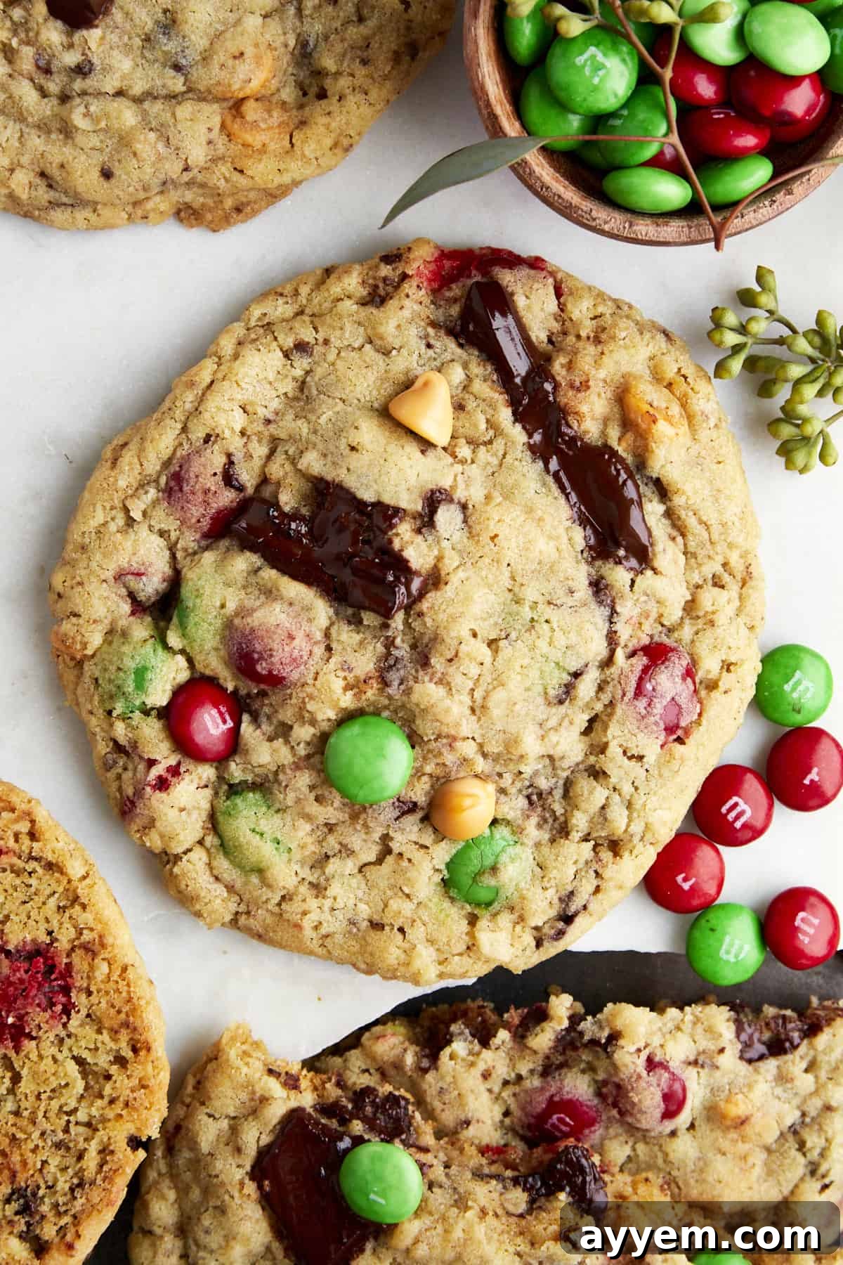 A large, perfectly baked Christmas monster cookie adorned with red and green M&M's, peanut butter chips, and chocolate chunks, sitting on a parchment-lined baking sheet. It showcases a soft, chewy texture perfect for holiday celebrations.