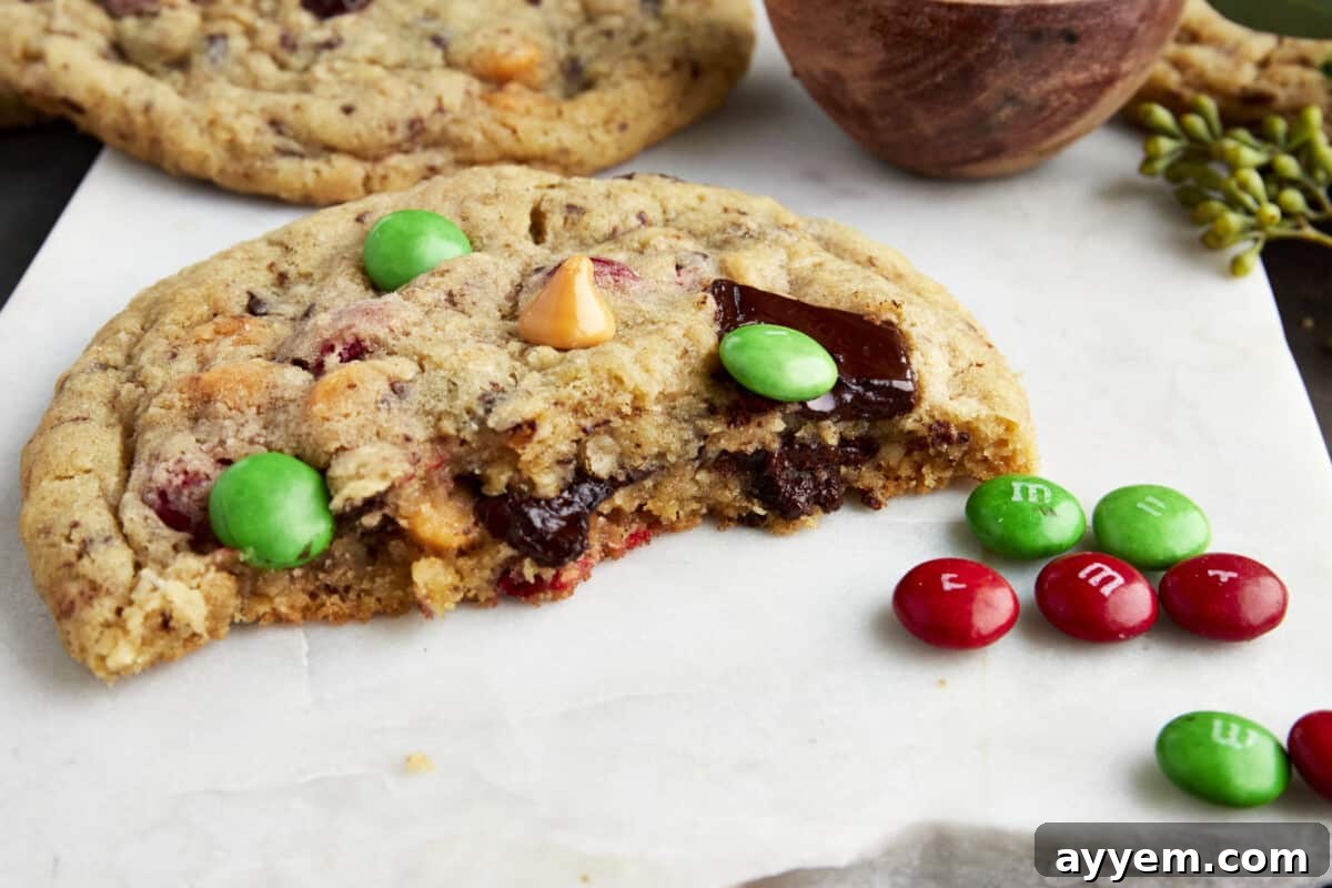 A half-eaten Christmas monster cookie revealing its soft, chewy interior filled with M&M's, peanut butter chips, and chocolate chunks. Perfect for a cozy holiday treat.