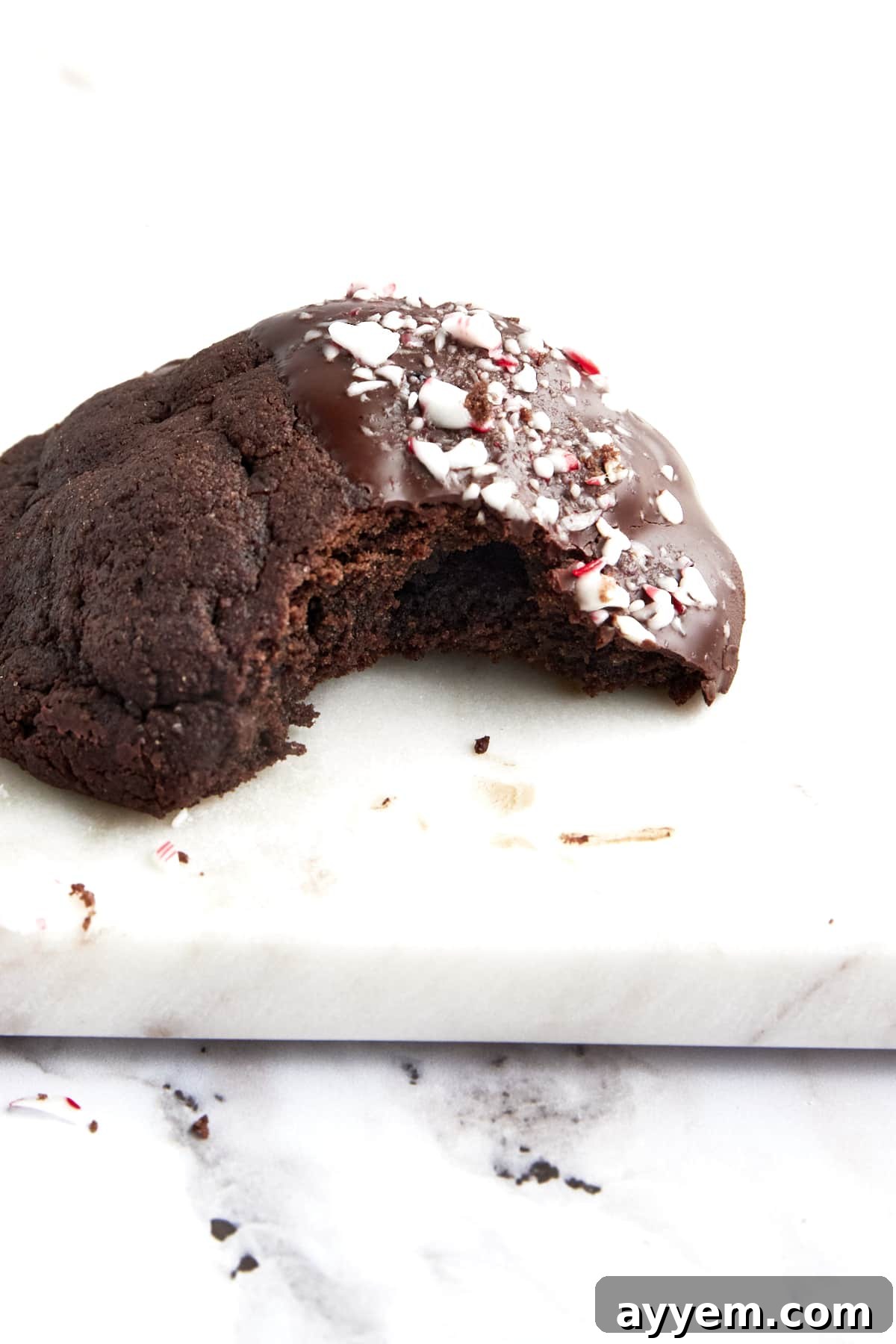 A single dark chocolate cookie dipped in white chocolate and adorned with crushed candy cane pieces, presented on a white surface.