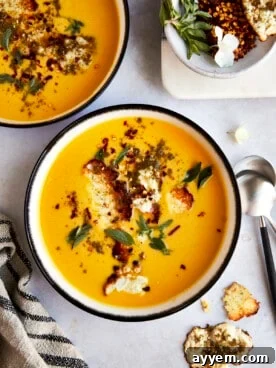 Two bowls of roasted butternut squash soup topped with crispy feta cheese and fresh herbs.
