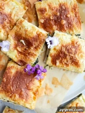 Golden brown squares of phyllo spinach pie, showcasing layers of crispy pastry and creamy filling.
