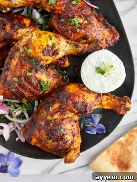 Crispy baked chicken tandoori legs served on a platter with a side of cooling tzatziki sauce.