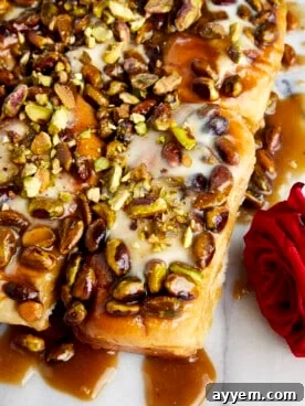 Golden, glossy baklava sticky buns arranged on a tray, drizzled with syrup and sprinkled with nuts.