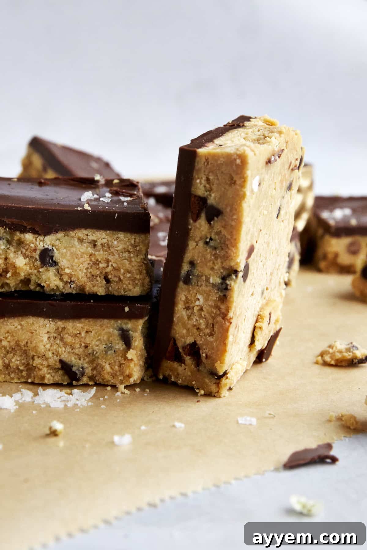 A perfectly sliced no-bake cookie dough bar with a rich peanut butter chocolate topping, next to two stacked bars.