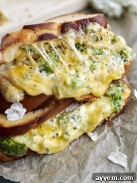 Two golden-brown roasted garlic and broccoli oven-grilled cheese sandwiches, stacked, with melted cheese and filling oozing out.