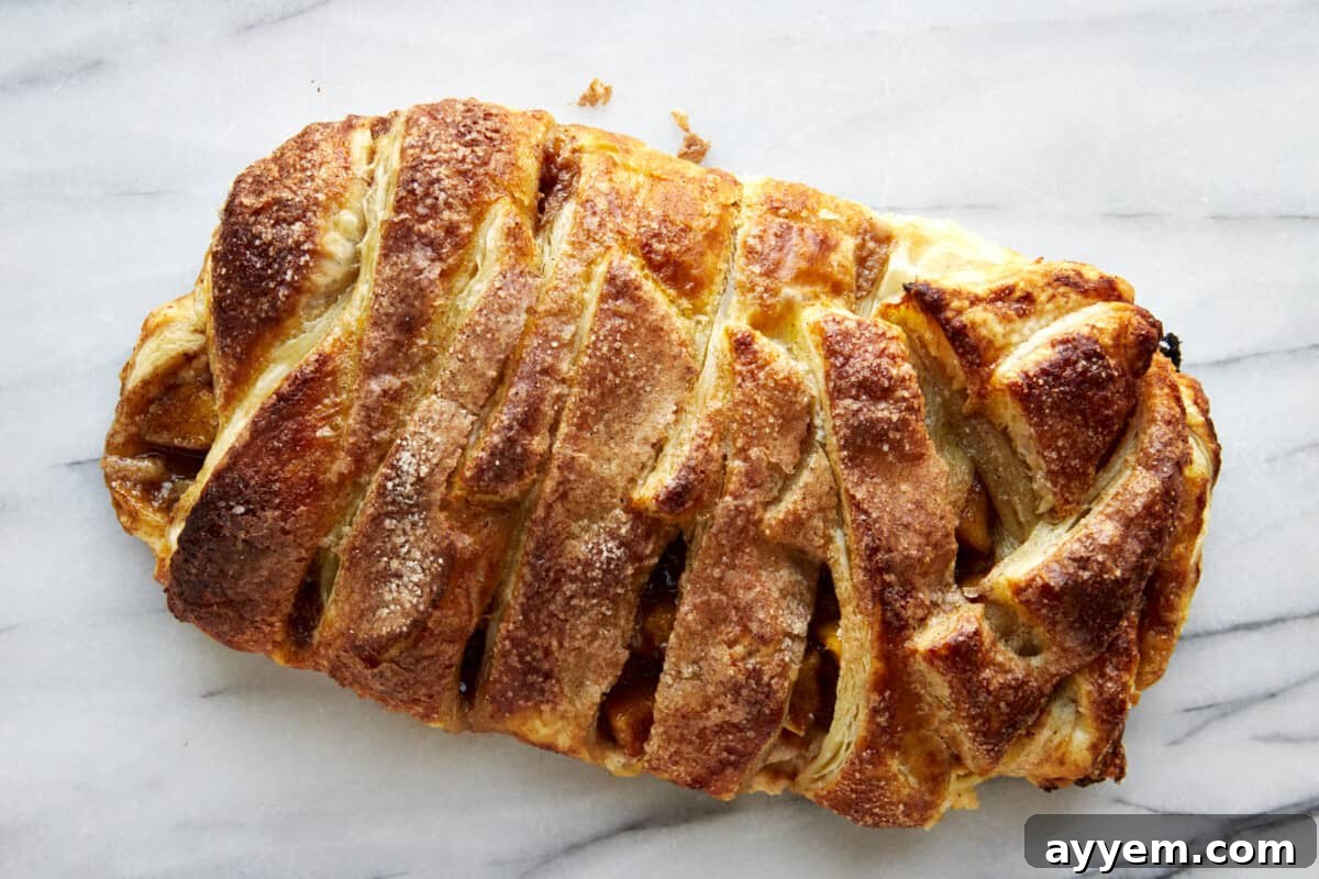 A freshly baked apple puff pastry braid, golden and puffed, cooling on a baking sheet, ready to be sliced.