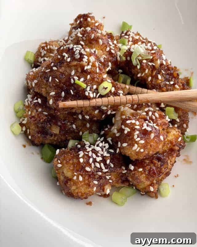 A bowl of honey garlic baked cauliflower with chopsticks grabbing a piece, ready to be enjoyed.